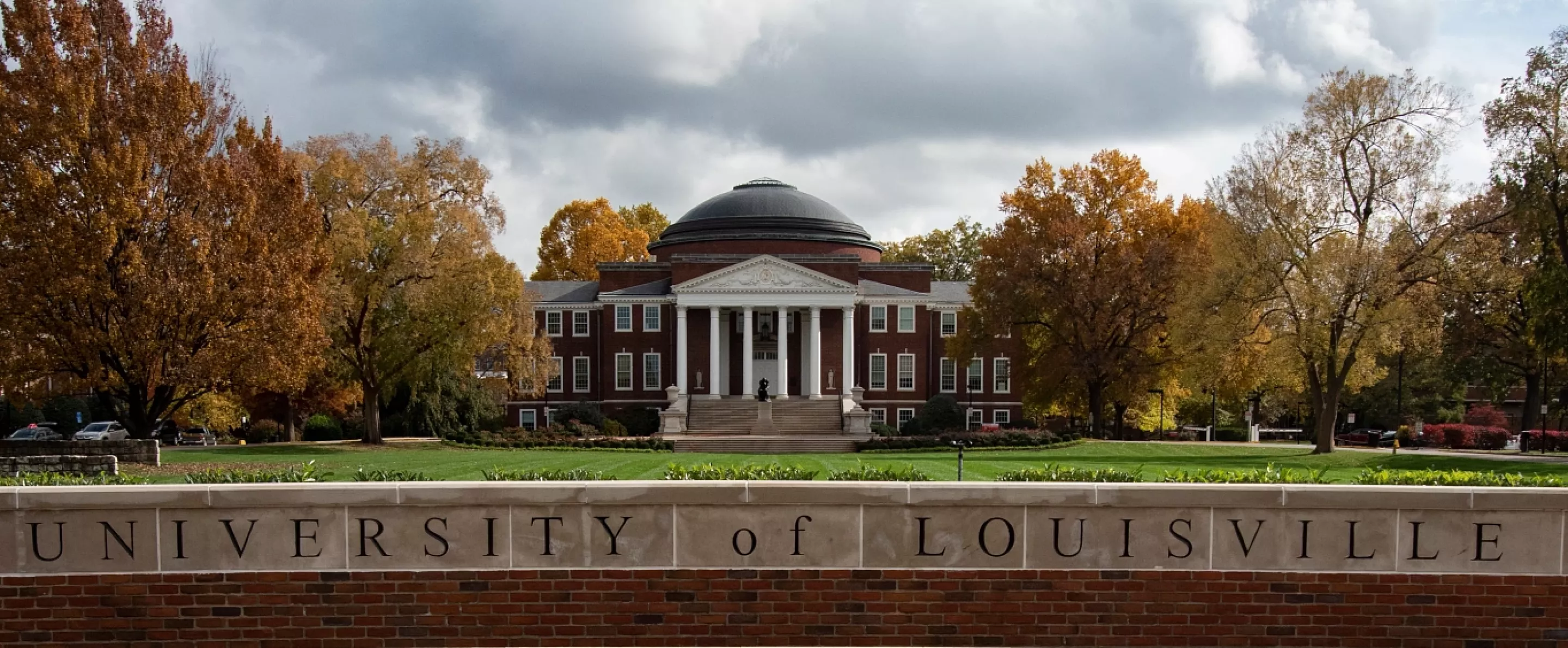 Wide-angle portrait of the exterior of Grawemeyer Hall and the Oval with the 3rd Street entrance sign and Minerva in the foreground
