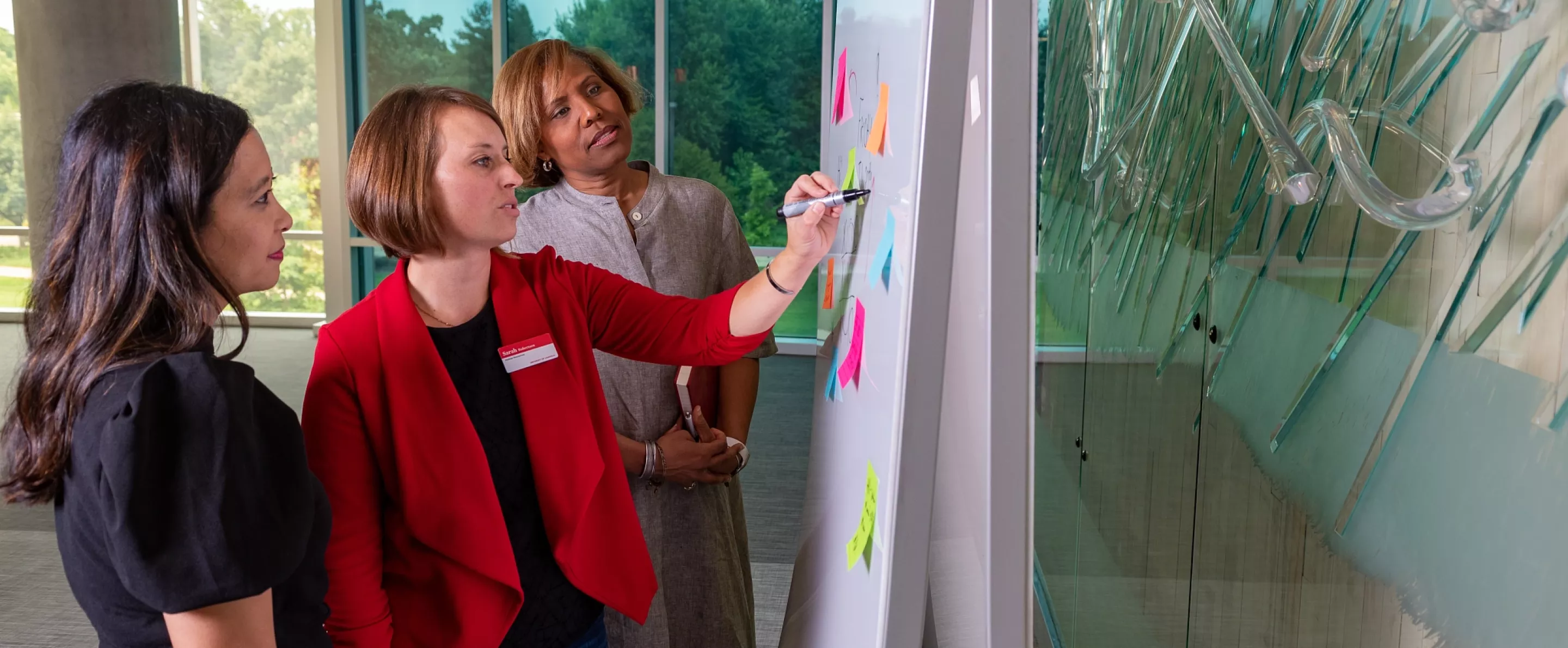 Three female employees collaborating in a whiteboard exercise using sticky notes