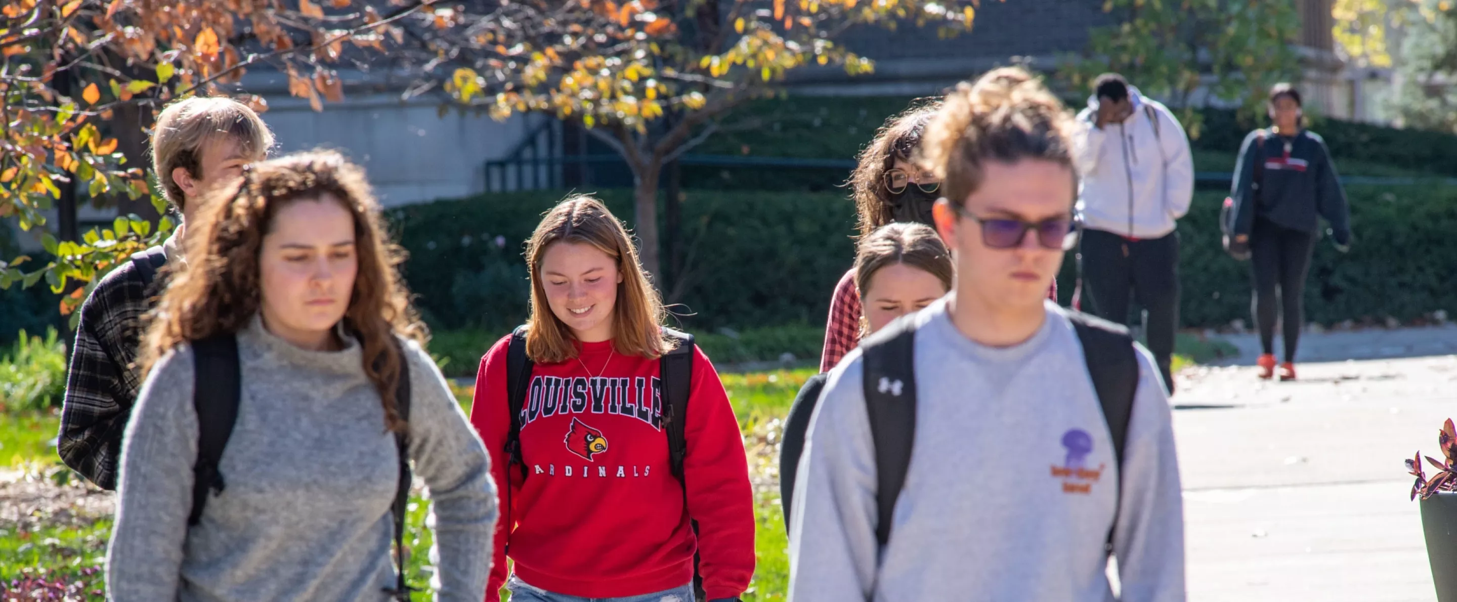 Students walking on sidewalk, female in the center is wearing a cardinal pullover.