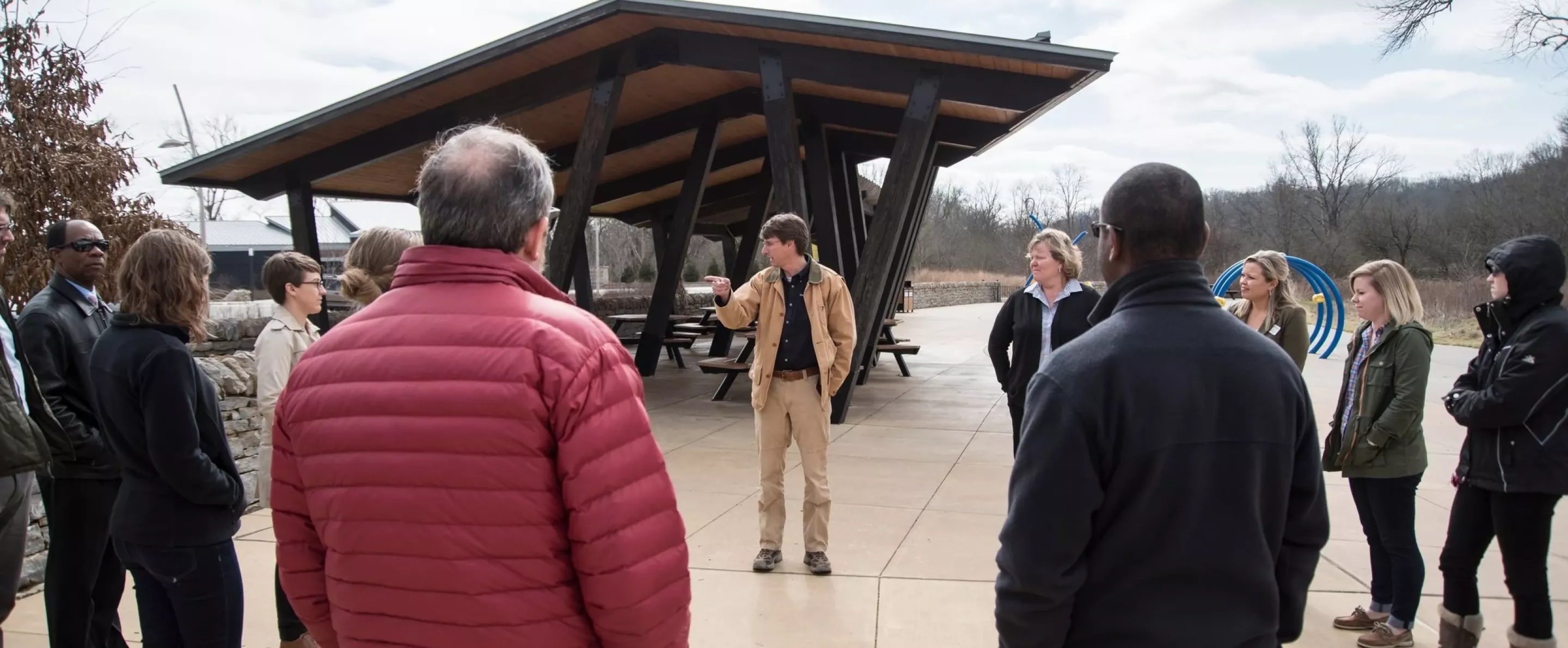Group of people standing outside at park watching instructor lead discussion.