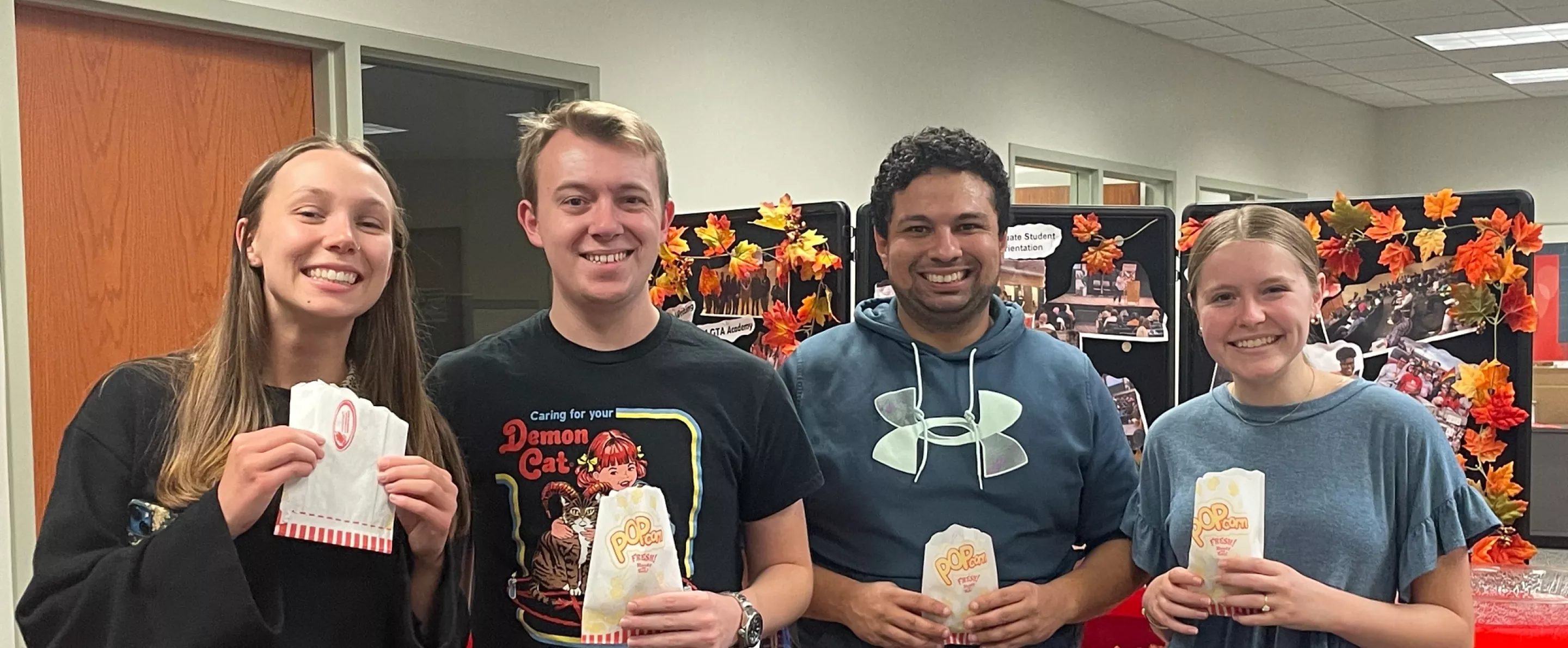 Four people holding bags of popcorn posing together.