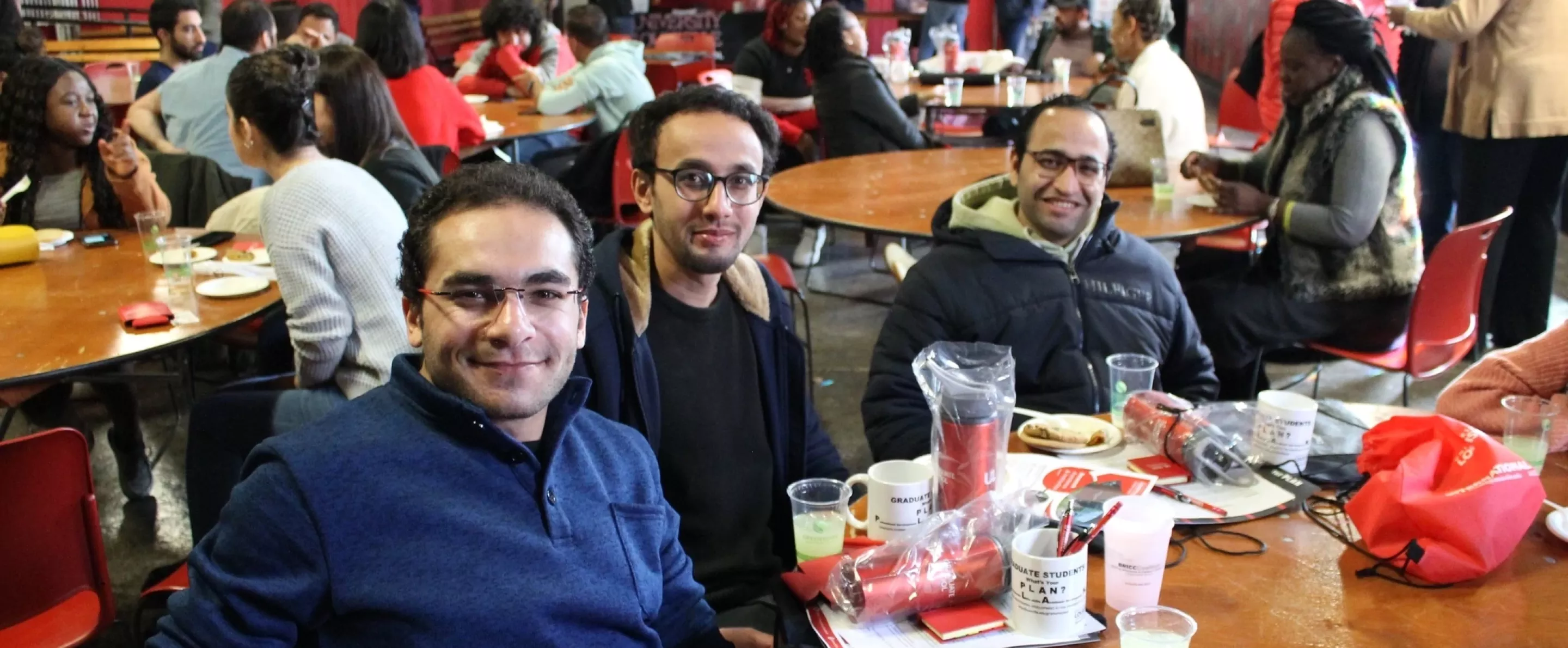 Three graduate students posing at a table with items and food in front of them.