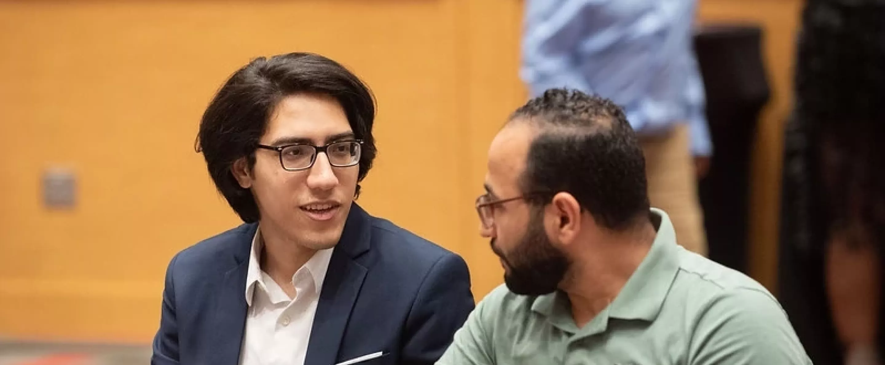 Two graduate students talking while sitting at a table during orientation.