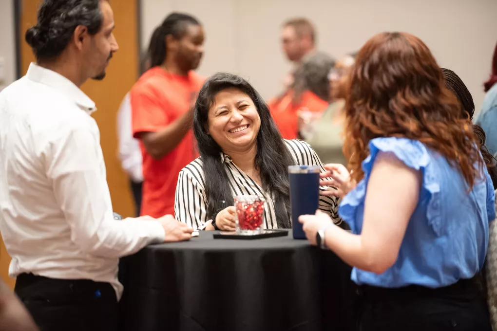 Graduate student laughing at a standing table with other students looking at her.