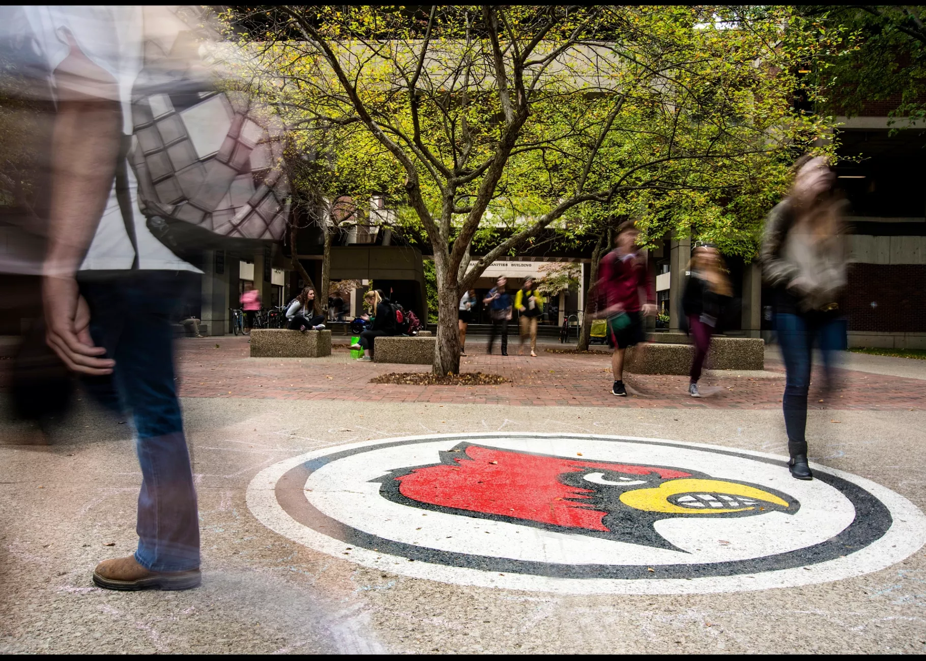 Blur of students walking by Cardinal Bird in front of Humanities