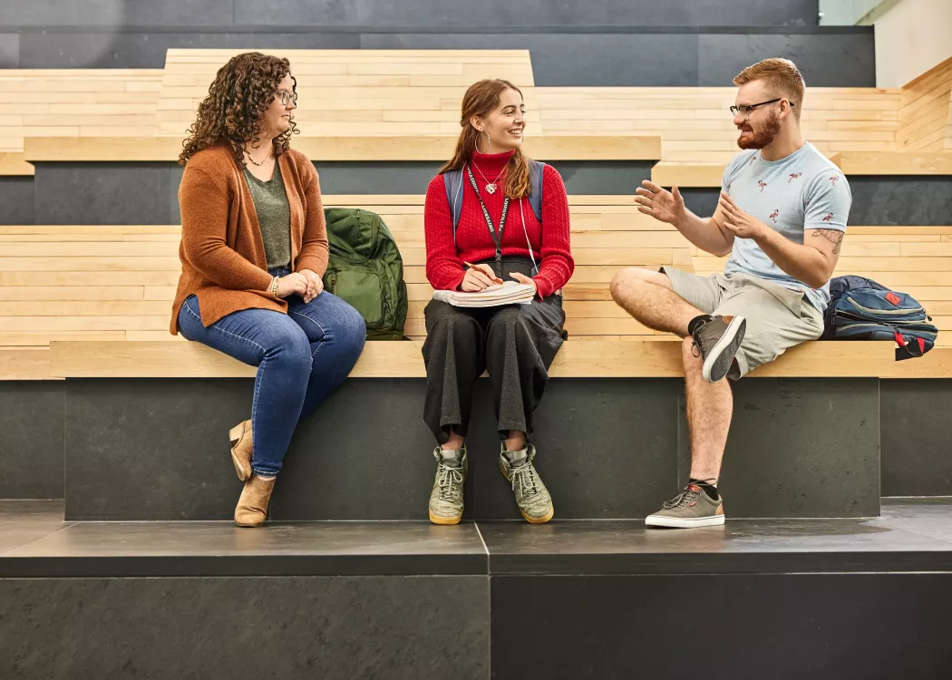 Alison Williams sitting on the wooden benches within the entrance of the Belknap Academic Building