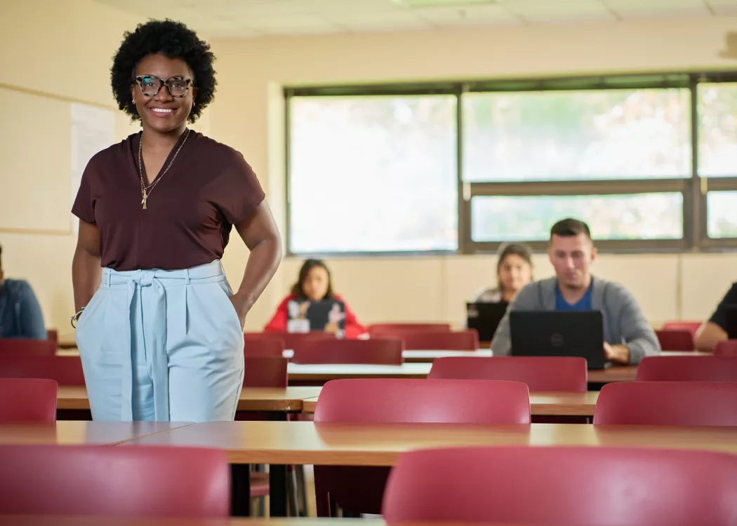 Female professor stands in front of her classroom and students posing for the campaign.