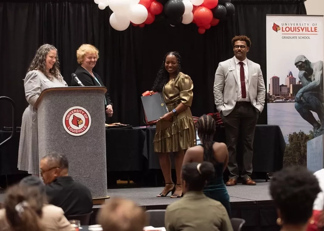 Person posing with award folder on decorated stage around three staff members presenting awards.