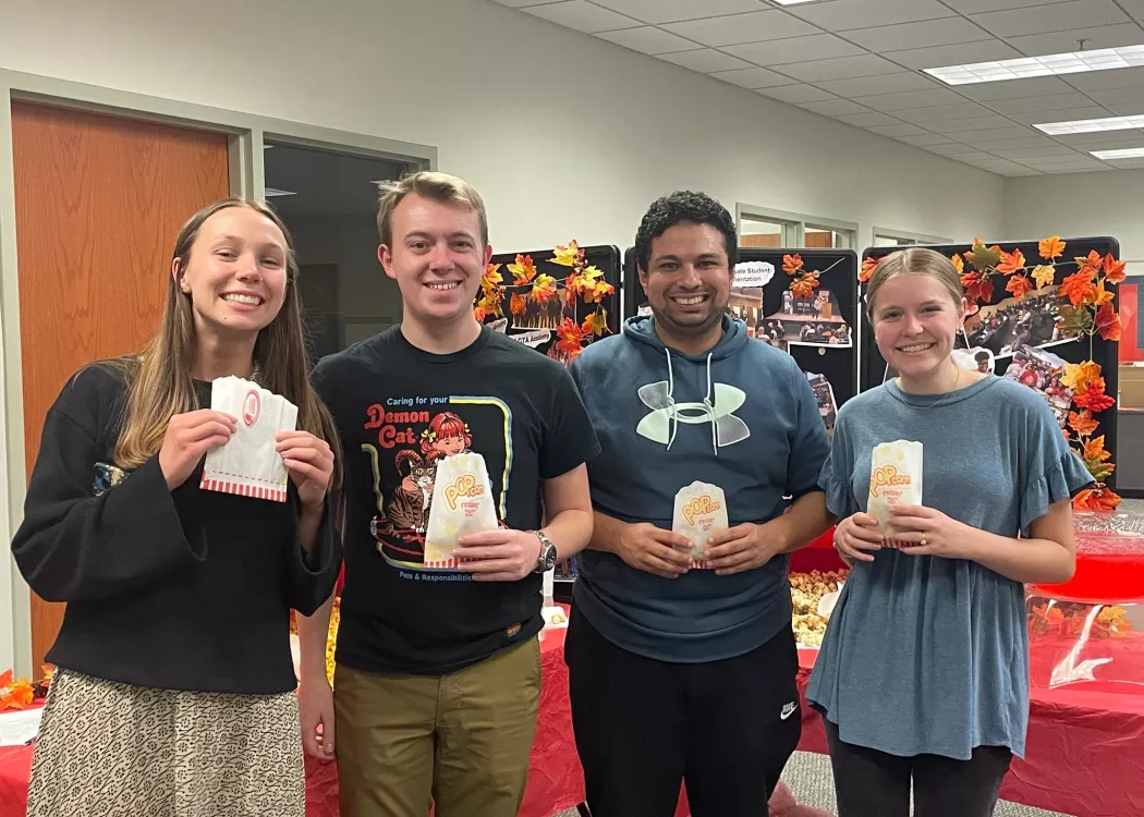 Four people holding bags of popcorn posing together.