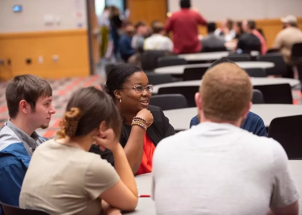 Graduate School staff member seated at a table, in discussion with students at school event.