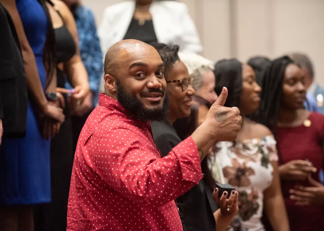 Graduate Student Jason Deakings giving thumbs up look at camera, people in background.