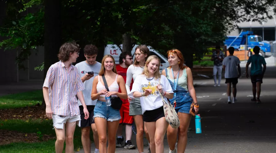 A group of students walking on campus looking at the camera and smiling