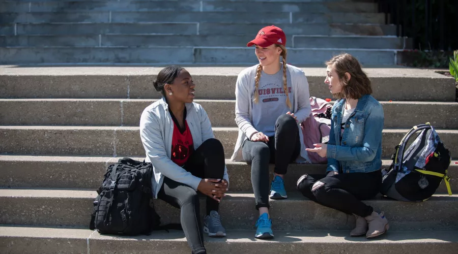 Three students hang out on steps of an academic building