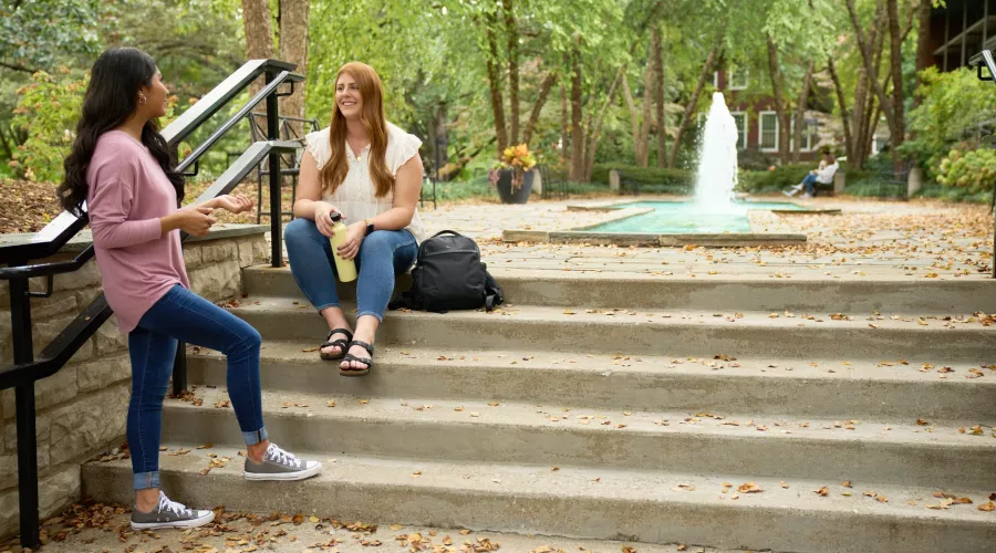 Two students talking on the stairs of the fountain area.