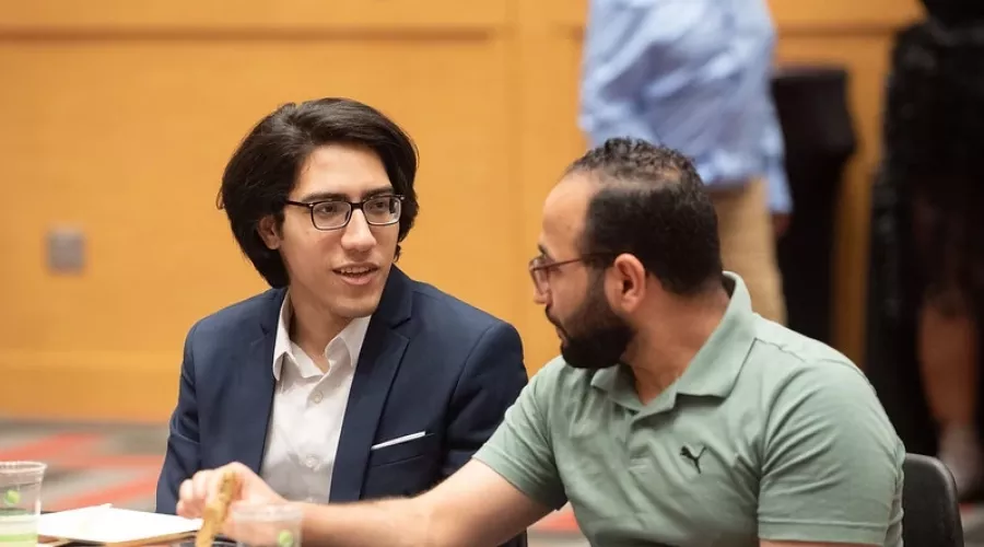 Two graduate students talking while sitting at a table during orientation.